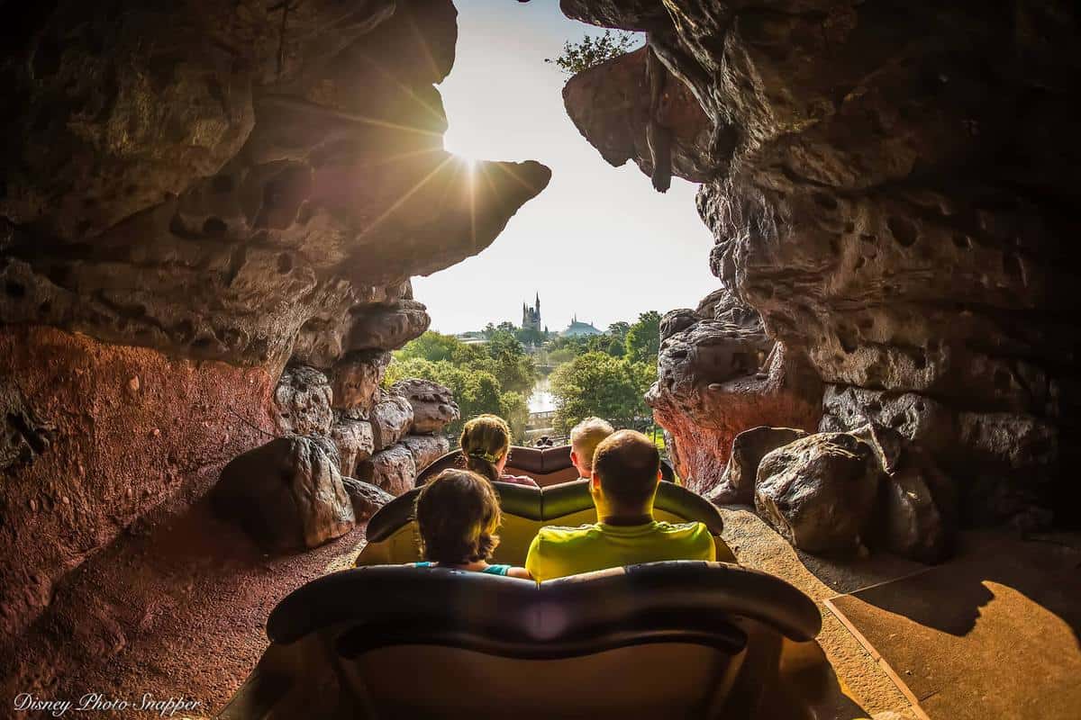 Guests splash down the Splash Mountain log flume, emerging from a rocky tunnel with Cinderella Castle gleaming in the distance.