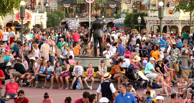 Guests fill the plaza at Disney World, gathering around the Partners statue amid festive park decorations on a busy day.