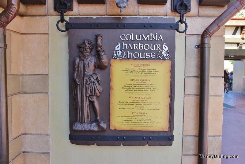 Columbia Harbour House menu sign with sailor mascot and tasty choices on a tan wall—classic Magic Kingdom dining charm.