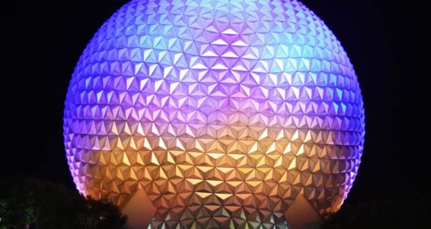 Spaceship Earth glowing at night in Epcot, illuminated with vibrant purple, blue, and gold lights against a starry sky.