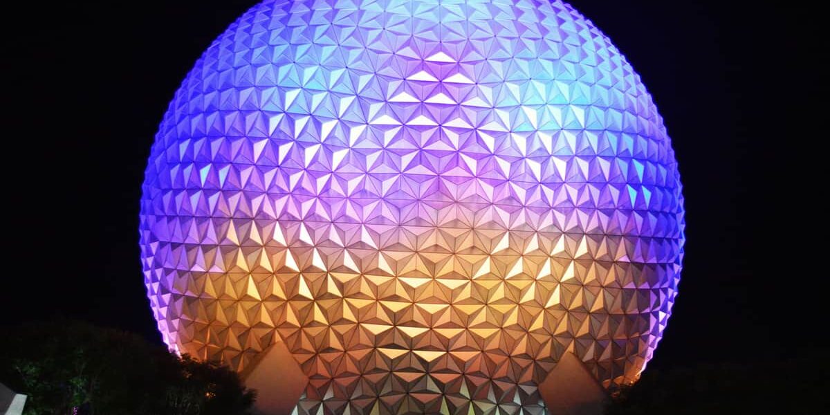 Spaceship Earth glowing at night in Epcot, illuminated with vibrant purple, blue, and gold lights against a starry sky.