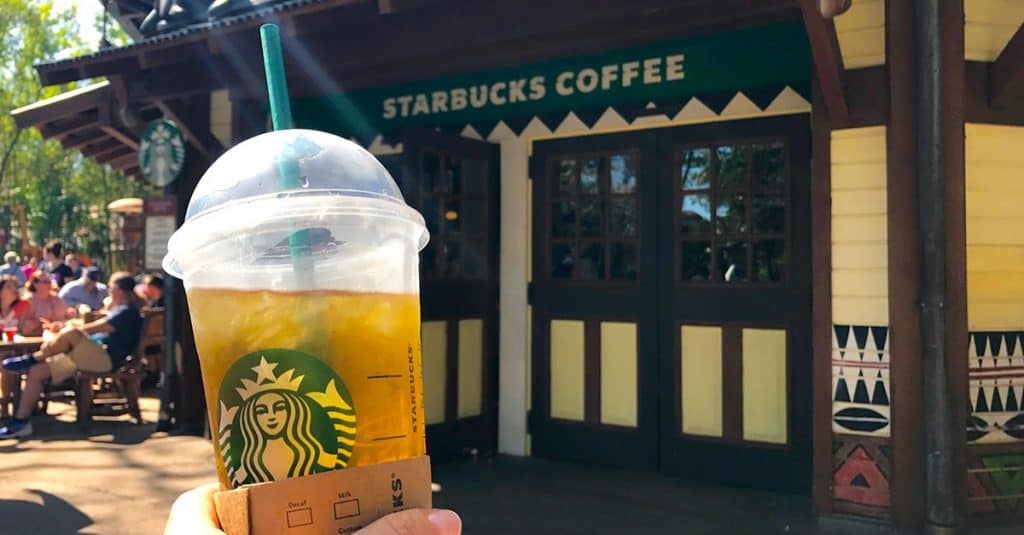 Starbucks iced drink held up in front of the Starbucks Coffee shop at Walt Disney World, glowing under sunny Florida skies.