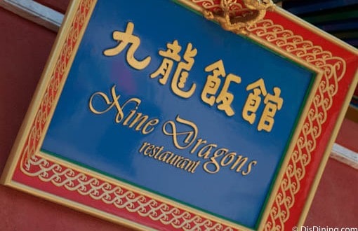 The iconic Nine Dragons Restaurant sign glows in gold on blue and red, welcoming EPCOT guests to an authentic Chinese feast.