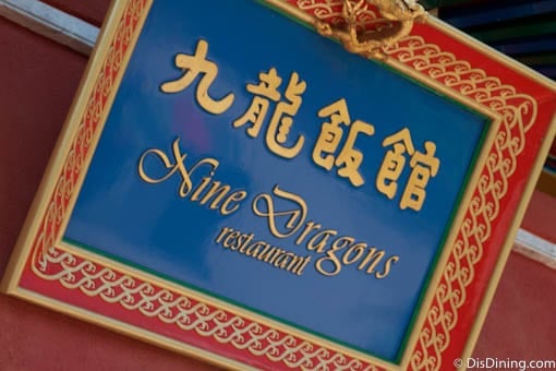 The iconic Nine Dragons Restaurant sign glows in gold on blue and red, welcoming EPCOT guests to an authentic Chinese feast.