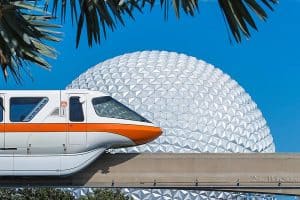 The Disney monorail glides by Epcot’s Spaceship Earth, framed by palms, beneath a vivid blue sky at Walt Disney World Resort.