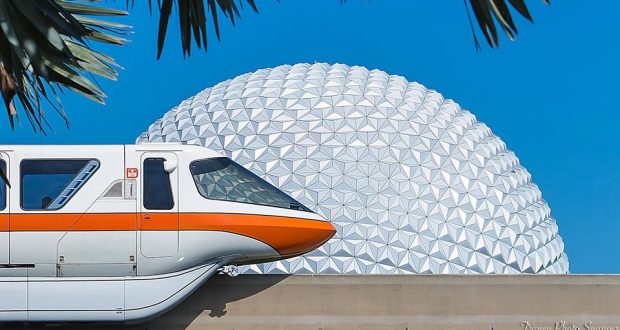 The Disney monorail glides by Epcot’s Spaceship Earth, framed by palms, beneath a vivid blue sky at Walt Disney World Resort.