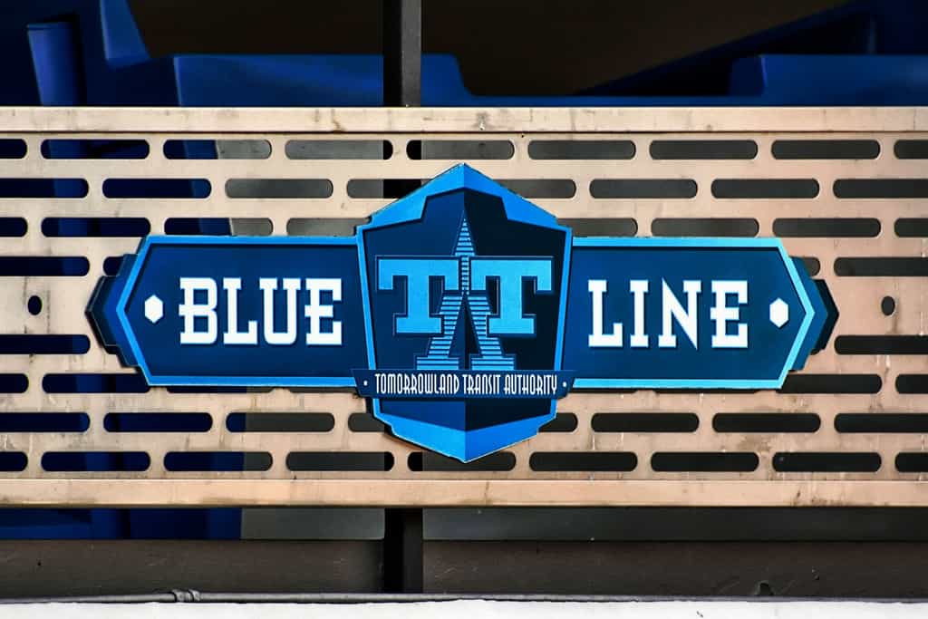 BLUE LINE" sign with Tarrant Transit Authority logo on a metal fence, blue seats behind—like Disney signs guiding park guests.