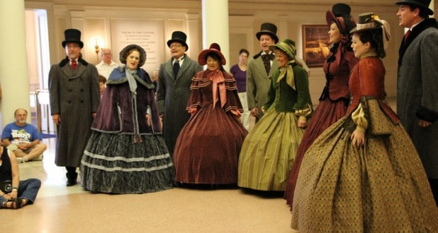 Victorian carolers perform inside The American Adventure at Epcot, entertaining casually dressed guests gathered around.