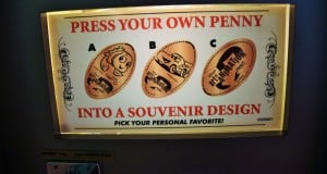 Colorful illuminated sign displays three exclusive pressed penny designs starring Disney’s *Cars* characters at Walt Disney World.