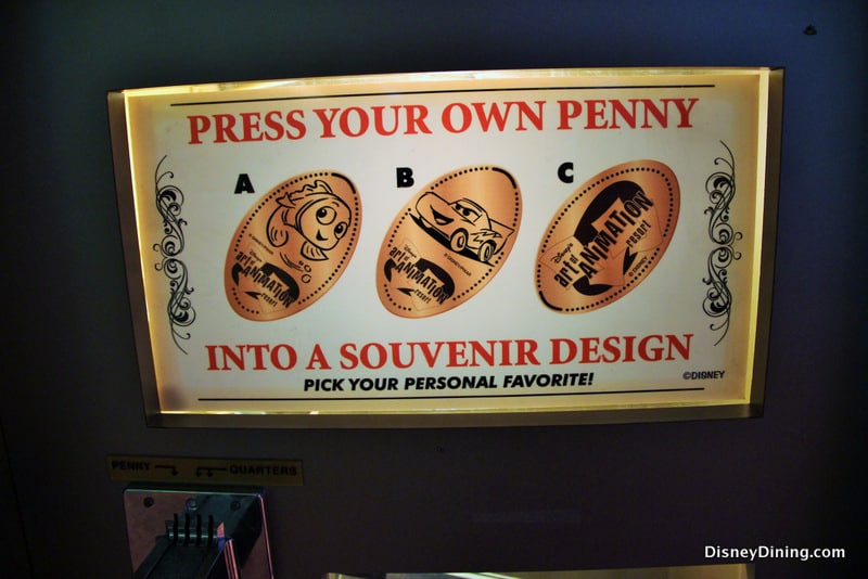 Colorful illuminated sign displays three exclusive pressed penny designs starring Disney’s *Cars* characters at Walt Disney World.