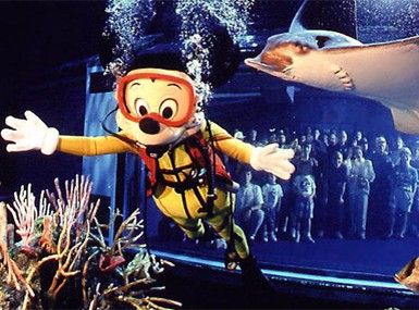 Mickey Mouse dives underwater in full scuba gear, swimming by coral as a shark glides behind—a Disney World aquatic adventure!.