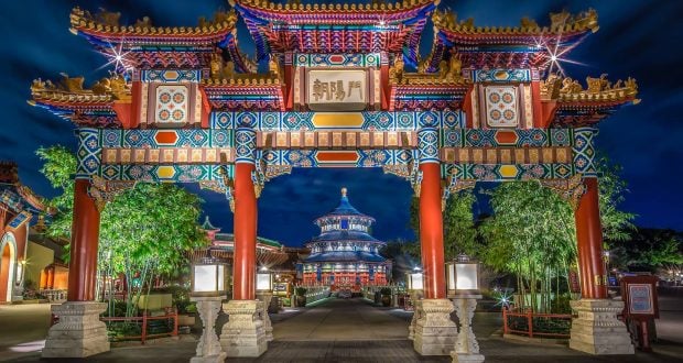 Epcot’s China Pavilion: vibrant, illuminated Chinese archway at night, bamboo-lined path, temple and glowing lights behind.