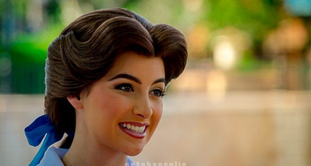 Belle greets guests with a radiant smile at Epcot, her brown hair styled beautifully with a charming blue ribbon—pure Disney magic.