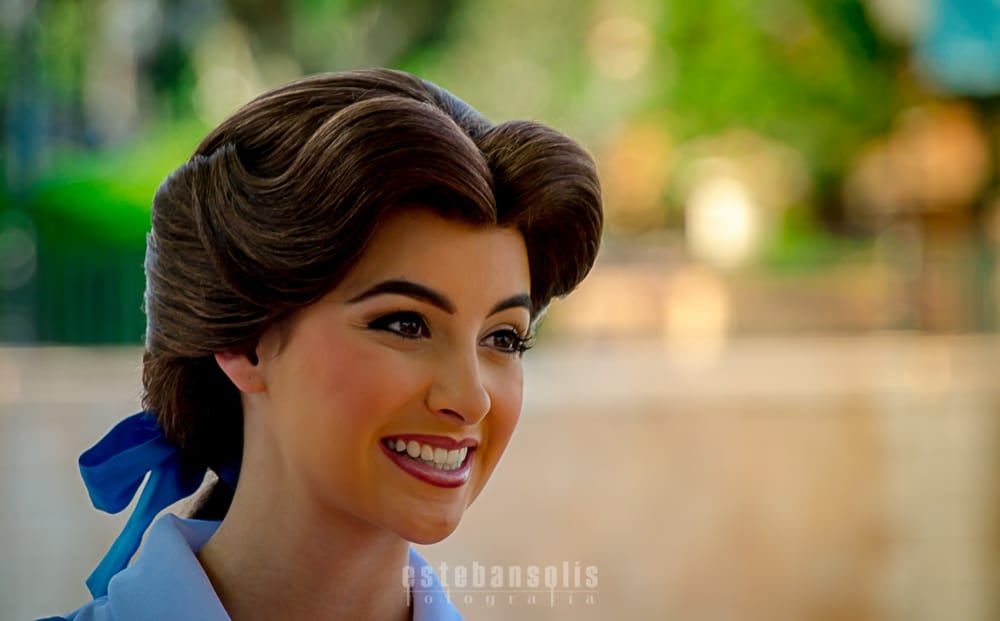 Belle greets guests with a radiant smile at Epcot, her brown hair styled beautifully with a charming blue ribbon—pure Disney magic.