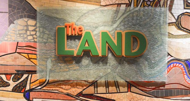 The LAND" sign on a sleek glass panel pops against a vibrant mosaic wall inside Epcot's iconic Land Pavilion at Disney World.