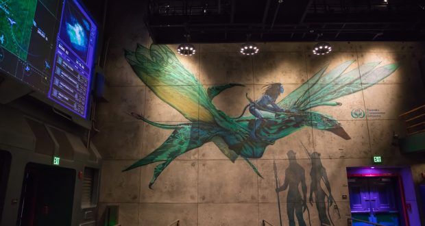 A vibrant mural of a guest riding a green, dragon-like creature brightens the queue at Walt Disney World’s indoor attraction.