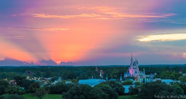 Sunset colors and sun rays create a magical atmosphere over Cinderella Castle at Walt Disney World, surrounded by lush trees.