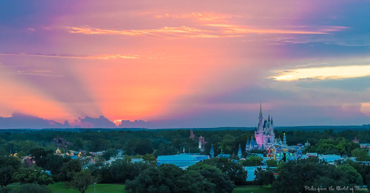 Sunset colors and sun rays create a magical atmosphere over Cinderella Castle at Walt Disney World, surrounded by lush trees.