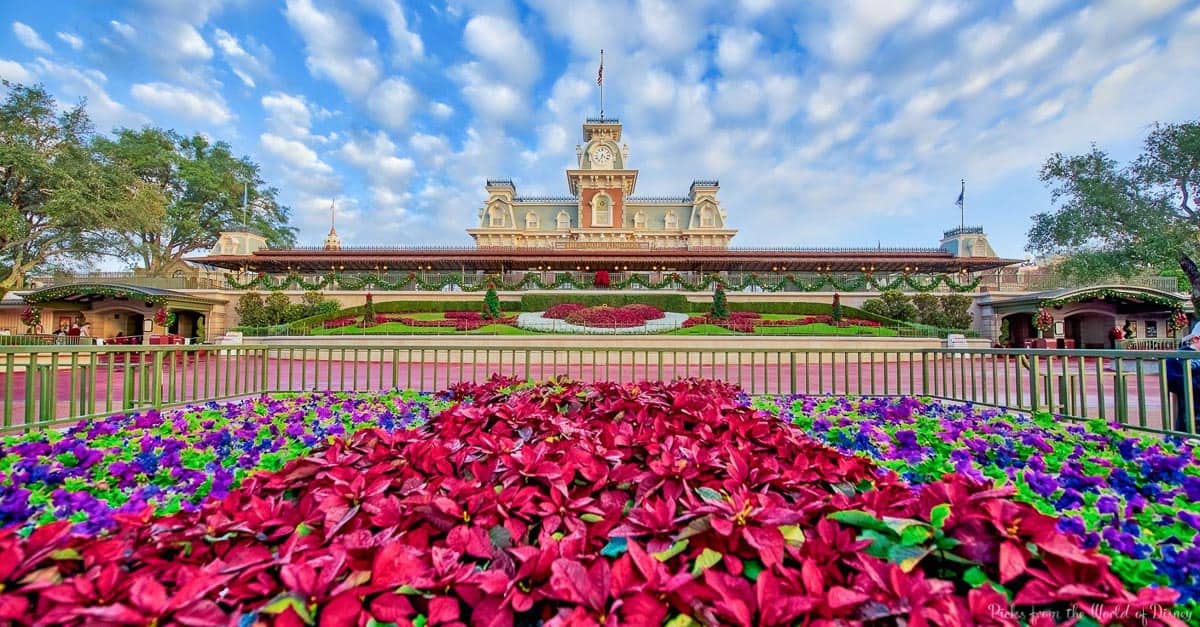 Vibrant flowers frame Magic Kingdom’s grand train station and iconic clock tower under sunny skies—a classic Disney welcome.