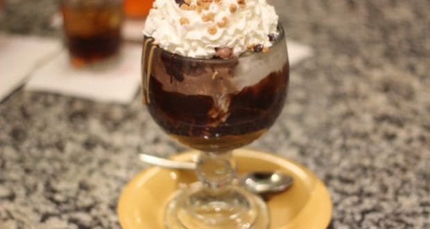 Chocolate sundae with whipped cream and sprinkles in a glass cup at Beaches & Cream Soda Shop, served on a yellow plate with a spoon.