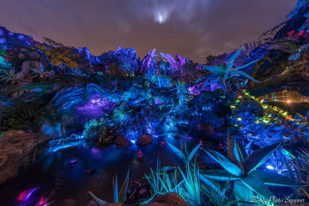 Pandora’s glowing alien landscape dazzles with vivid lights, rocky paths, and otherworldly plants beneath Disney’s magical night sky.