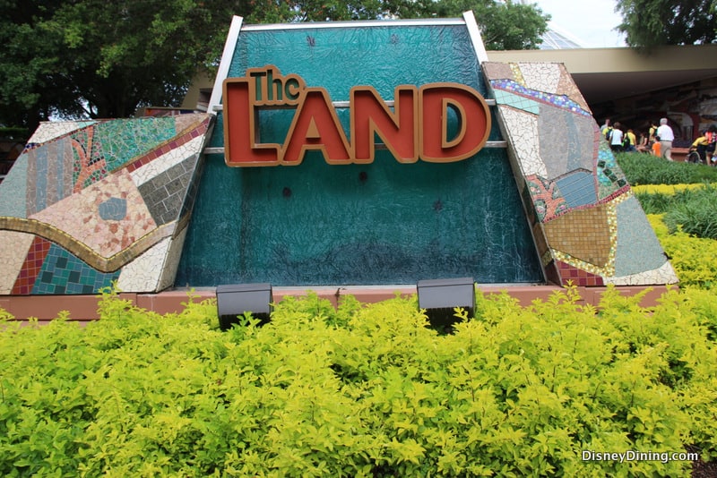 The Land's vibrant mosaic sign pops amid lush greenery at EPCOT, welcoming guests to discover its iconic Disney secrets.