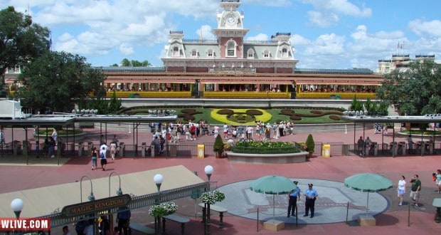 Magic Kingdom entrance with colorful Mickey Mouse floral display, excited guests, and Main Street train station—Disney magic awaits!.