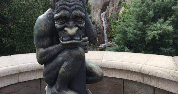 A gargoyle clings to a column amid lush greenery and a waterfall, channeling the enchanted vibes of iconic Disney venues.