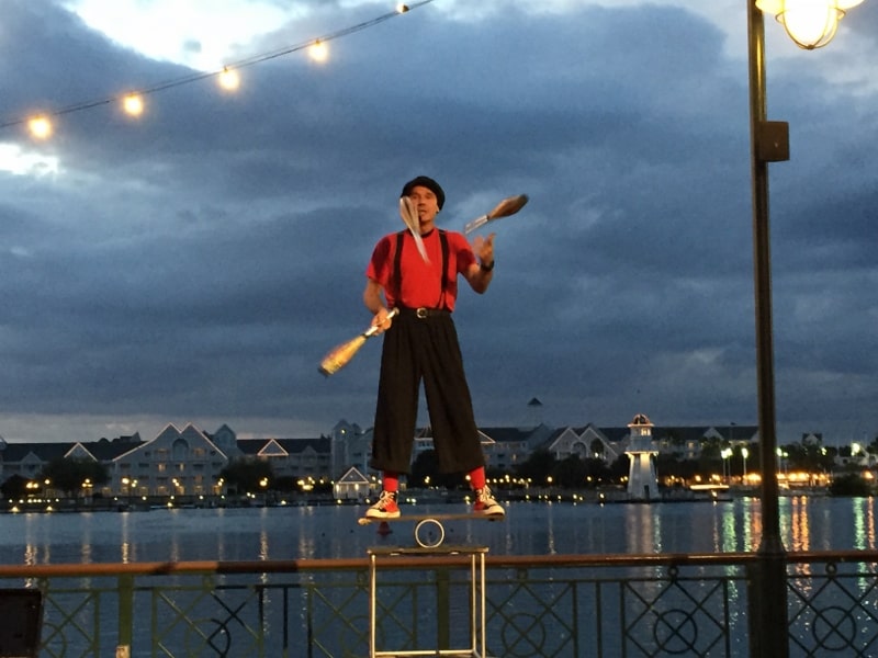A vibrant performer in red juggles by the waterfront at dusk, bringing Disney Springs-style thrills—no ticket required.