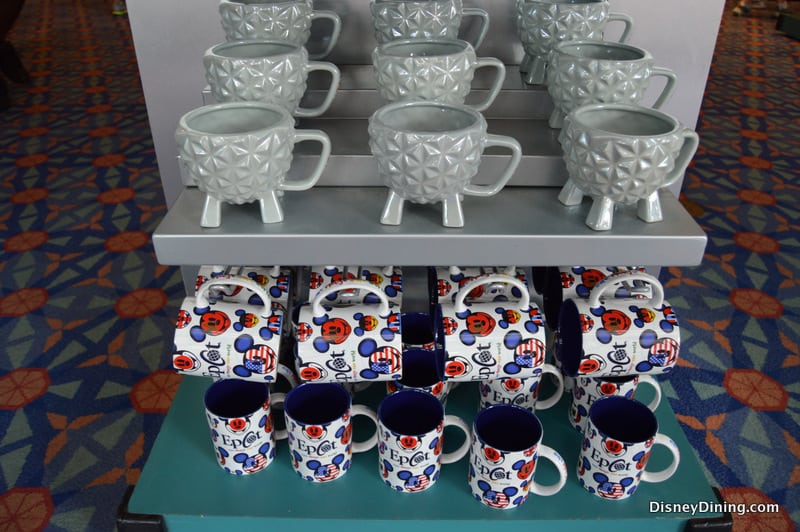 Gray EPCOT mugs sit above vibrant Walt Disney World mugs featuring Mickey Mouse and EPCOT logos, a must for Disney park fans.