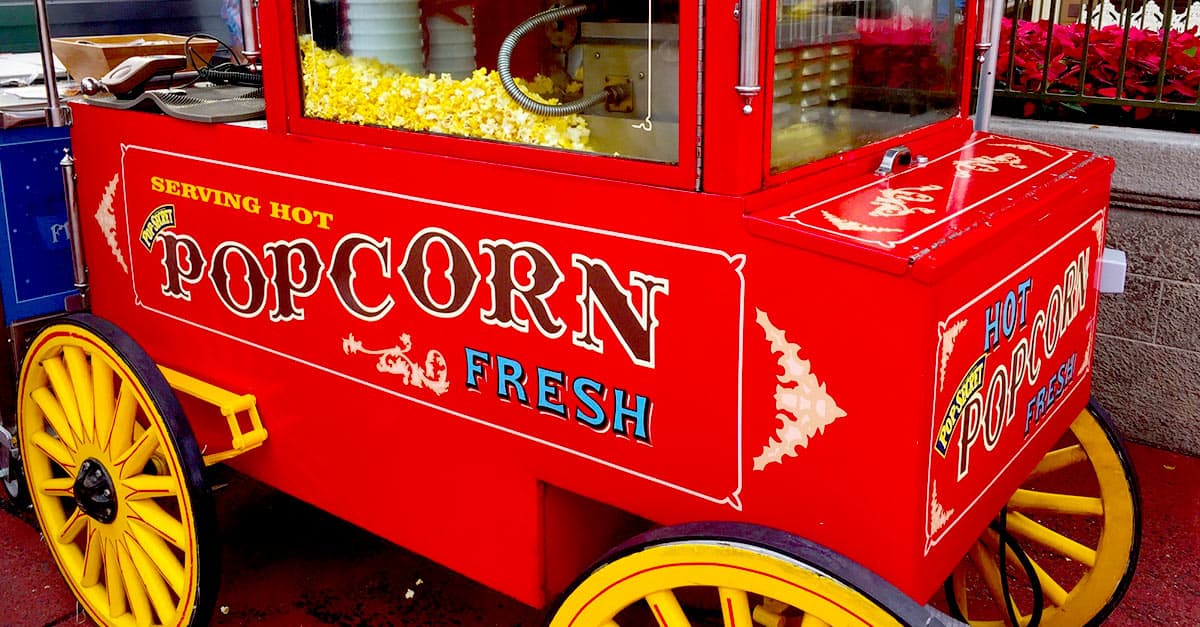 Classic Disney snack vibes: a bright red popcorn cart with yellow wheels and fun lettering, serving fresh popcorn at Disney World.