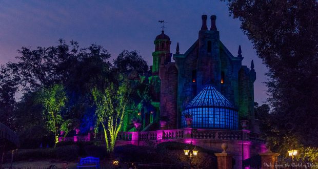 The Haunted Mansion glowing at dusk with vibrant colors, gothic spires, and eerie trees—an iconic Magic Kingdom nighttime must-do.