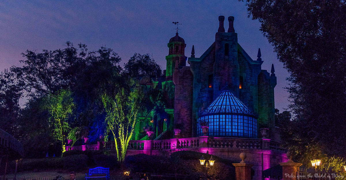 The Haunted Mansion glowing at dusk with vibrant colors, gothic spires, and eerie trees—an iconic Magic Kingdom nighttime must-do.
