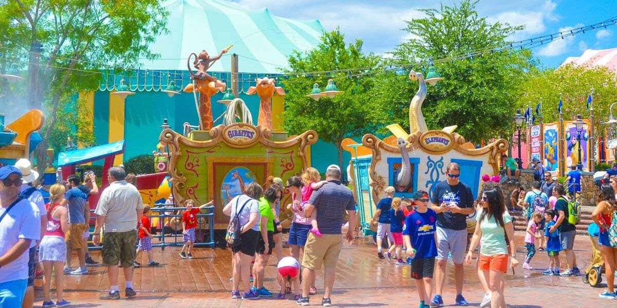 Guests stroll through a vibrant, circus-themed section of Disney World, soaking in the park’s lively atmosphere on a sunny day.