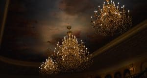 Three ornate chandeliers glow beneath a dreamy, cloud-painted ceiling, evoking the enchantment of Disney World dining magic.