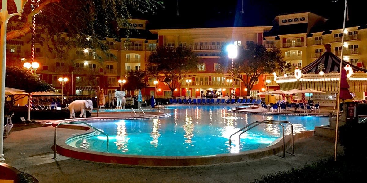 Disney resort pool glowing at night, with a whimsical white carousel horse and lounge chairs creating magical vacation vibes.