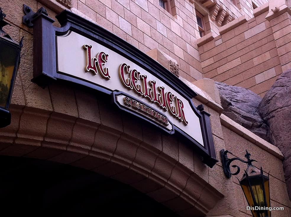 Le Cellier Steakhouse sign welcomes Disney foodies above a stone archway, with lanterns lighting the way to this fan-favorite eatery.