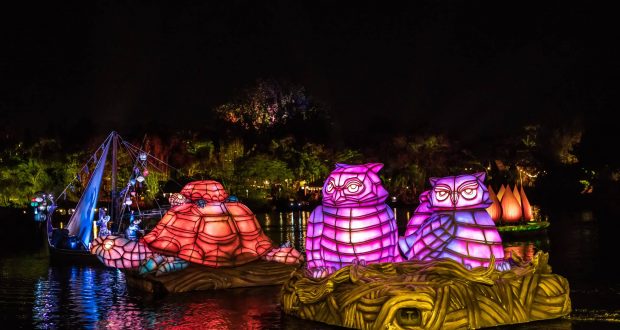 Animal-shaped floats glow in pink, purple, and orange as they glide down the river at night during Animal Kingdom’s vibrant show.