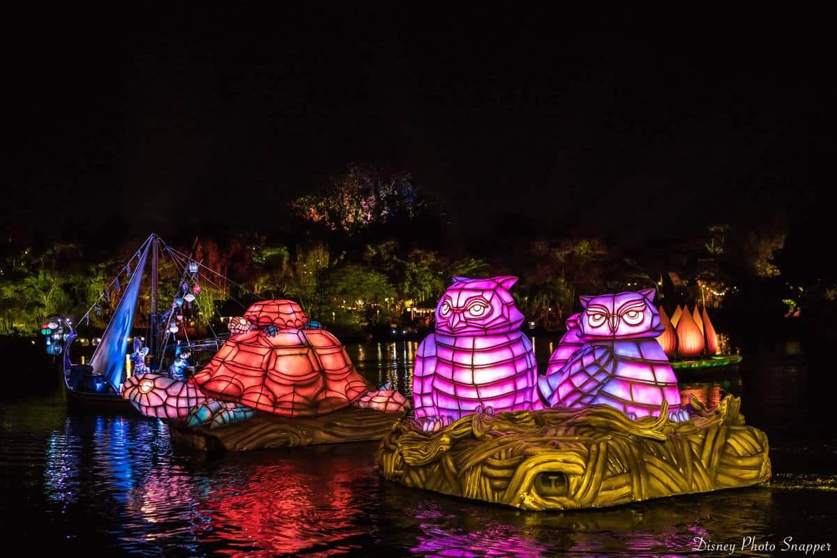 Animal-shaped floats glow in pink, purple, and orange as they glide down the river at night during Animal Kingdom’s vibrant show.