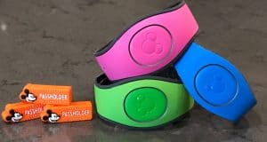 Three vibrant Disney Magic Bands and two Passholder orange Mickey magnets on gray—must-haves for any Disney Parks fan!.
