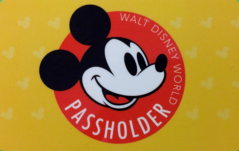 Bright yellow Disney World Passholder card featuring Mickey Mouse's face in a red circle, unlocking annual member perks.