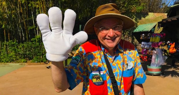 Mickey Mouse greets guests in a vibrant shirt and hat, waving with his signature glove and sharing Disney World tips for grandparents.