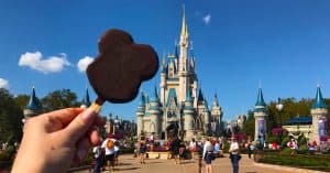 Enjoying the iconic Mickey Mouse ice cream bar with Cinderella Castle in the background at Disney World.