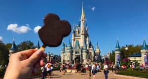 Enjoying the iconic Mickey Mouse ice cream bar with Cinderella Castle in the background at Disney World.