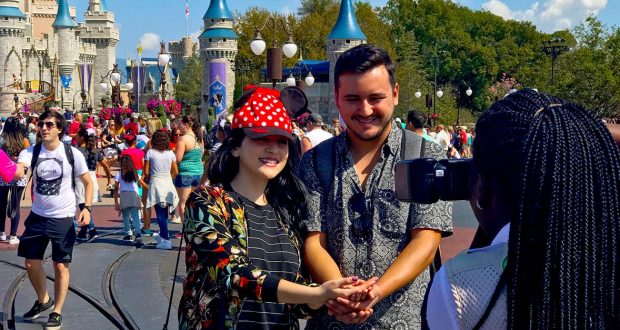 Guests smile for a Memory Maker photo in front of Cinderella Castle at Disney World, surrounded by lively crowds and a pro photographer.