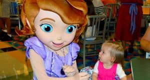 A young guest in pink gazes up at a Disney princess with big blue eyes and brown hair, embodying the magic of character dining.