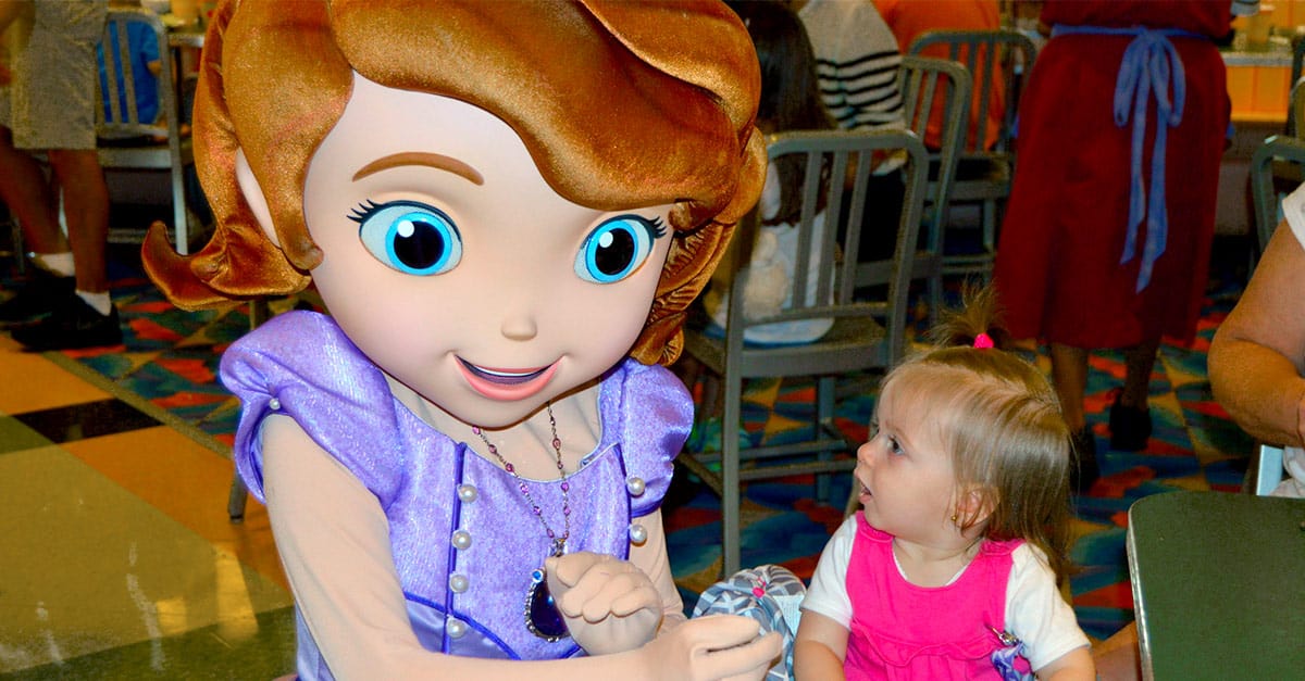 A young guest in pink gazes up at a Disney princess with big blue eyes and brown hair, embodying the magic of character dining.