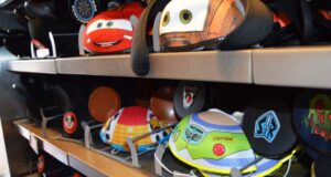Colorful Disney-themed Mickey Mouse ear hats, including designs inspired by Cars and Toy Story, are displayed on metal shelves in a store.