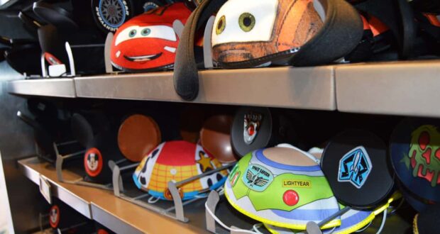 Colorful Disney-themed Mickey Mouse ear hats, including designs inspired by Cars and Toy Story, are displayed on metal shelves in a store.