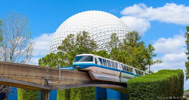 Disney’s iconic monorail glides past Spaceship Earth at Epcot, framed by lush trees and a brilliant blue sky.